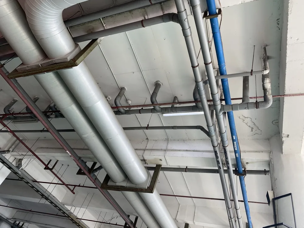 Commercial plumbing and heating pipework run beneath a warehouse ceiling